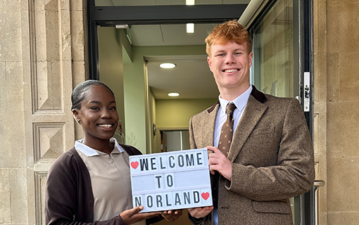 a male and a female student holding a sign that says Welcome to Norland at an open day