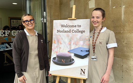 Two Norland Nanny students stood in front of a sign that says 'Welcome to Norland College' at an open day