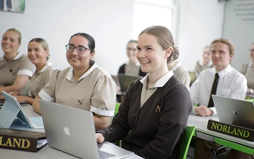 Norland students in formal uniform in a lecture, smiling to camera with laptops and folders